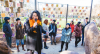 Person with a microphone talking in front of a gathering of people in an outdoor art installation space