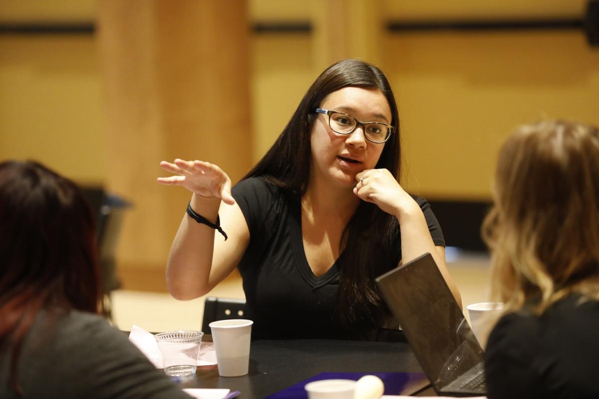 A person is engaged in conversation and is gesturing with their hand. The table also has disposable cups and some other small items. The background is indoors with warm-toned walls and blurred details.