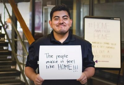 A student holding a sign that says "The people make it feel like home!" for our Home Away From Home Campaign that asks why students love the Kelly ECC