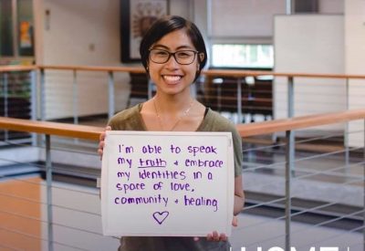 A student holding a sign that says "I'm able to speak my truth & embrace my identities in a space of love, community, and healing." for our Home Away From Home Campaign that asks why students love the Kelly ECC