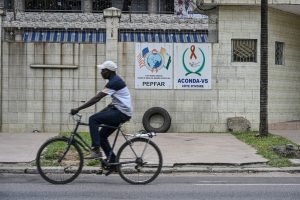 A man on his bike passing through two signs on a wall for PEPFAR in Abidjan, Ivory Coast