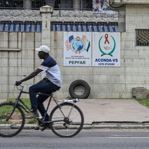 A man on his bike passing through two signs on a wall for PEPFAR in Abidjan, Ivory Coast