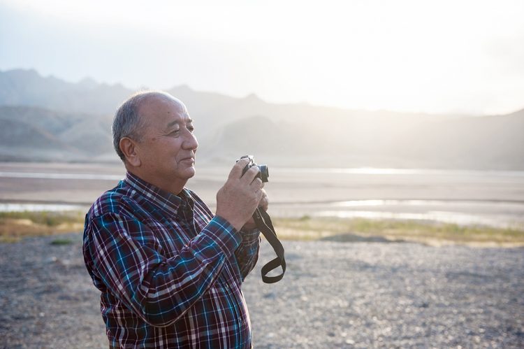 Older Chinese man holding a camera on the beach