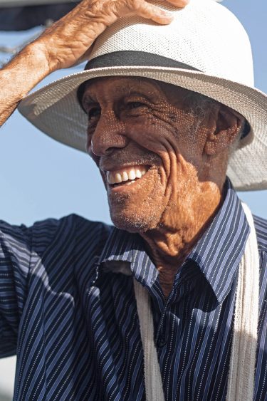 Older black man smiling and tipping his white hat