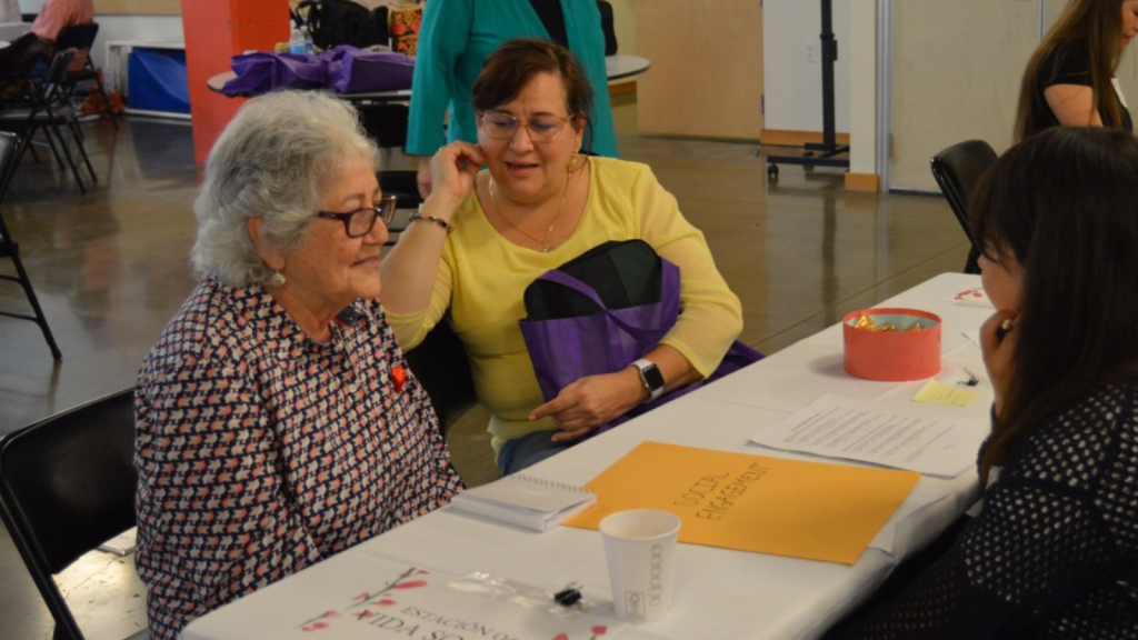 Three people gather around a table to discuss social engagement at the Brain Health and Community Resource Fair.