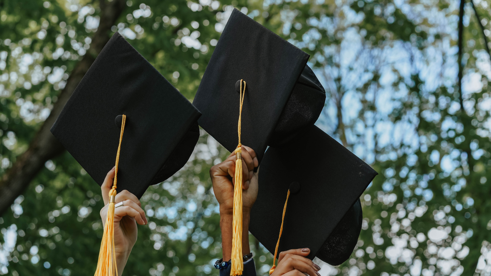 Students hold graduation caps up.