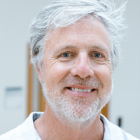 Profile photo of Chris Coward smiling in front of a gray, neutral background.