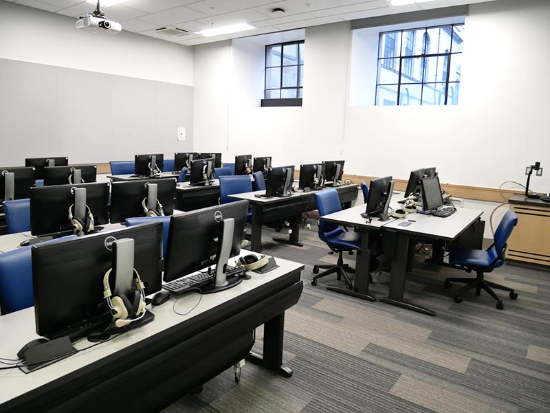 Photo of empty classroom with many computers for use by students. Taken from the door.