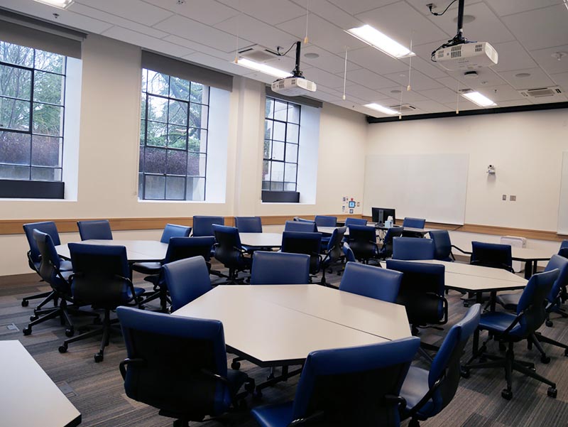 Empty classroom with 6 large tables for five students to sit at each.