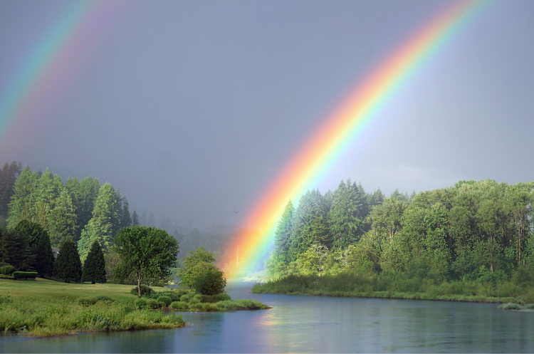 A double rainbow above a river and forest