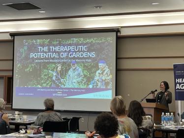 woman presents to an audience from a slide that reads: the therapeutic potential of gardens