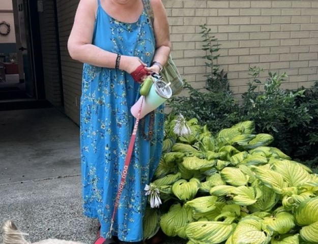 Woman in blue summer dress walking a service dog on a leash