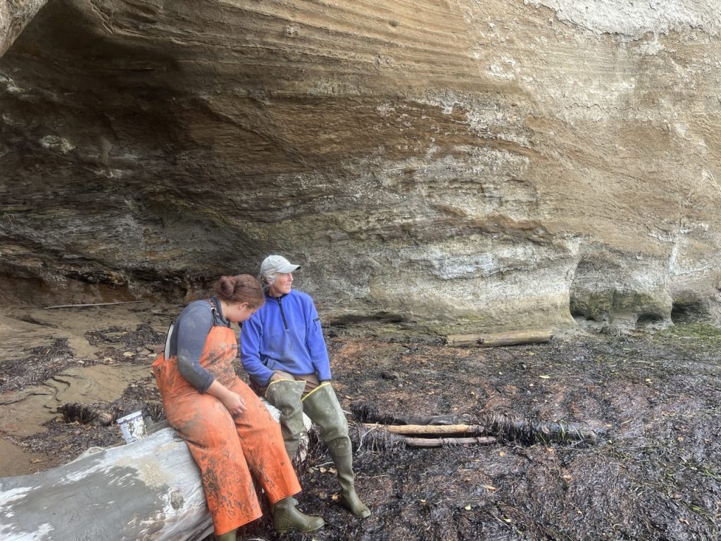Two scientists covered in mud sit on a log.