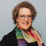 A smiling white-presenting woman with glasses and a colorful scarf.