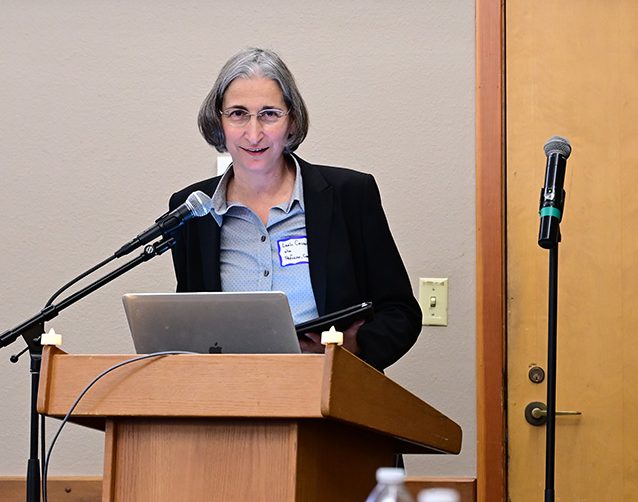 Women with short gray hair and black blazer at podium.