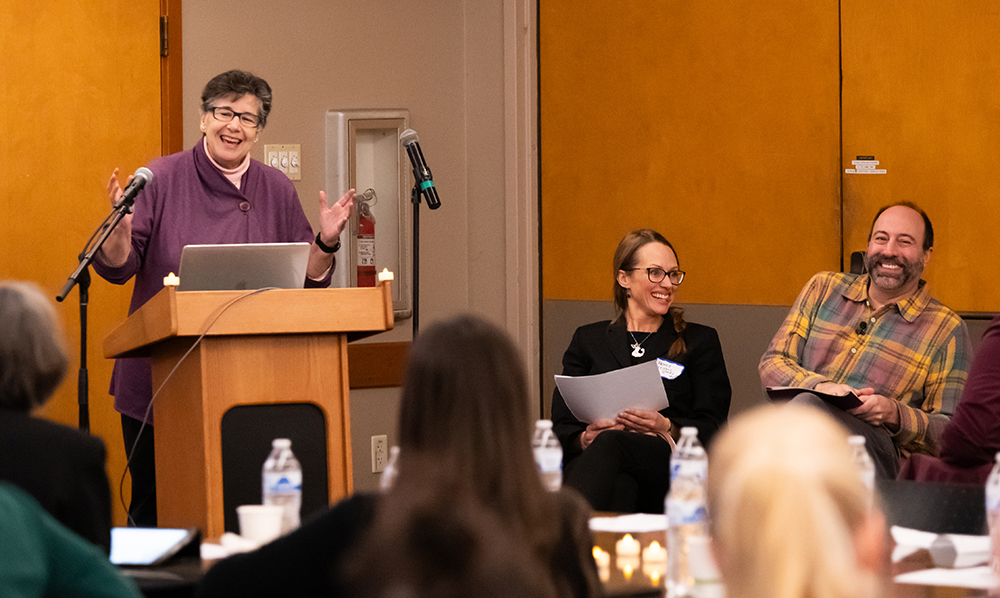 President Ana Mari Cauce waves hands enthusiastically while Monika Sengul-Jones, in black, and Ryan Calo, in plaid, laugh.