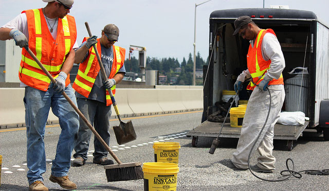 Three crew men manually performing highway maintenance