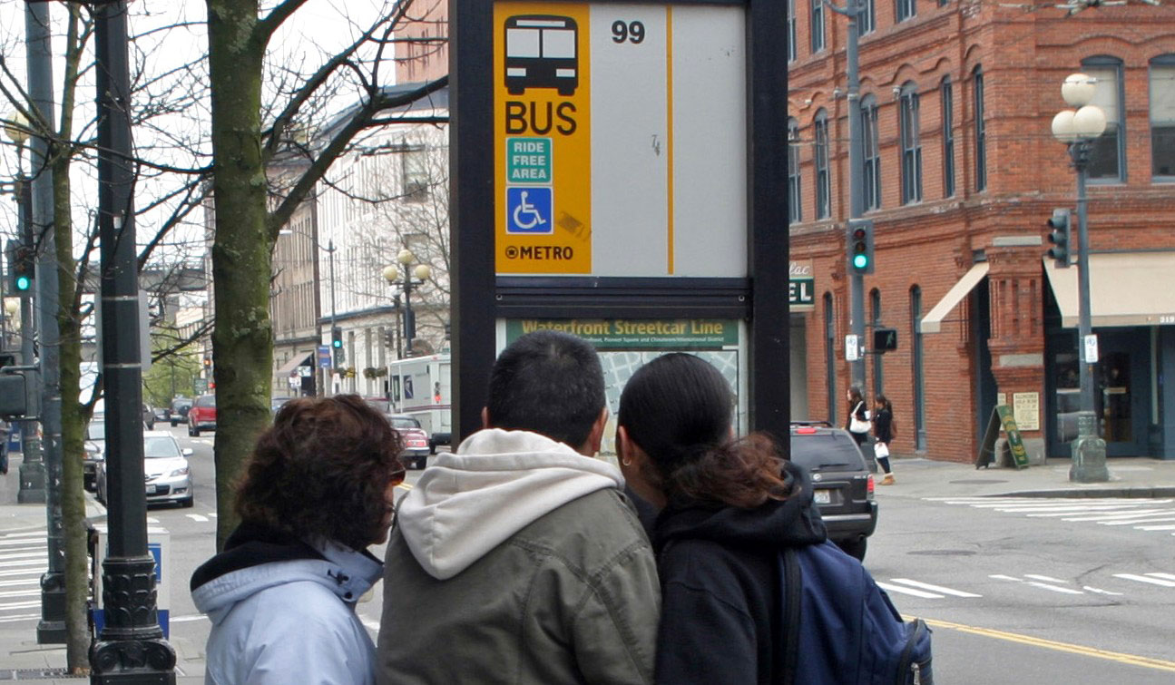Transit riders reading a bus schedule sign
