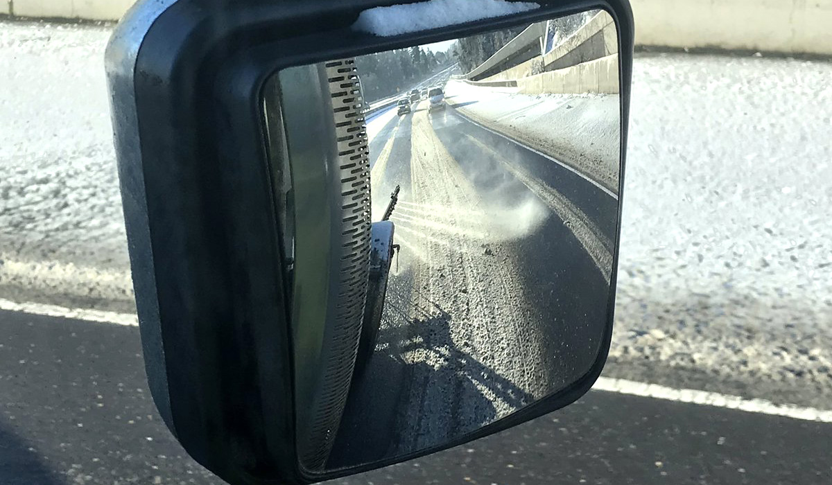 Roadway de-icer being applied, as seen in the truck's rear view mirror