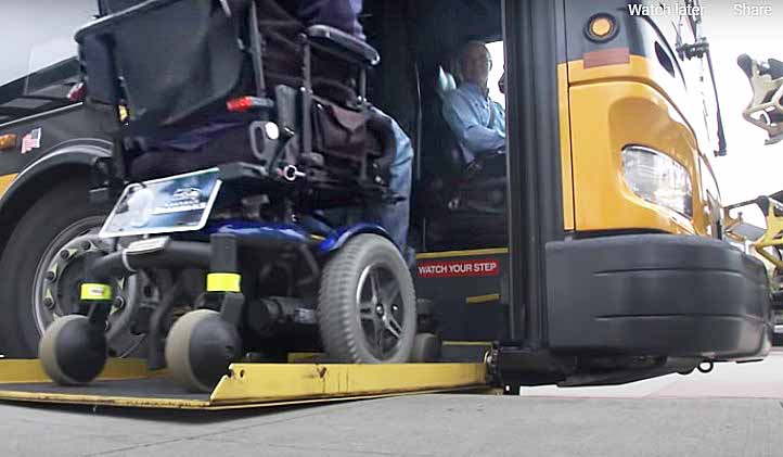 A bus patron in a motorized chair moves onto a bus lift.