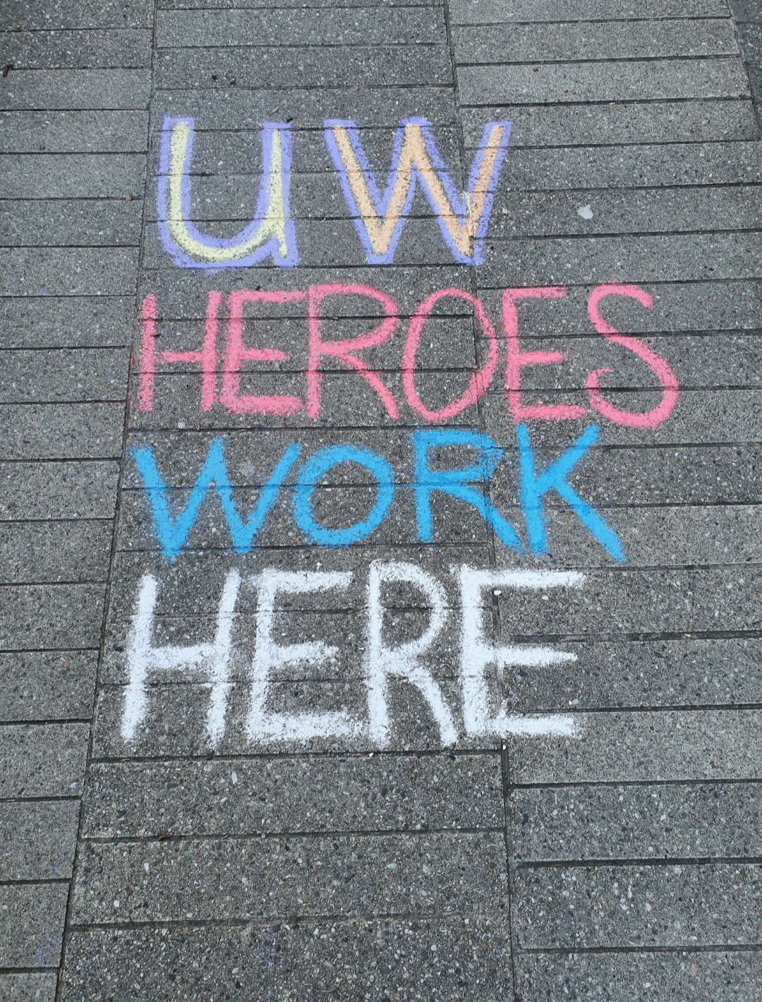 Sidewalk graffiti reading: UW Heroes Work Here.