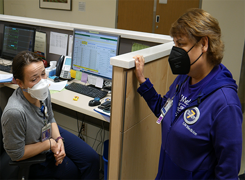 Cindy Sayre wearing an N95 mask speaking with a seated nurse