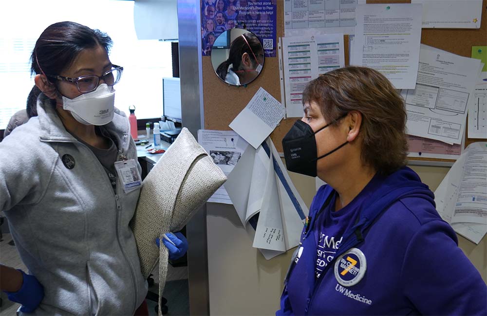 CNO Cindy Sayre wearing an N95 mask and talking with a masked nurse standing in front of a cork board.