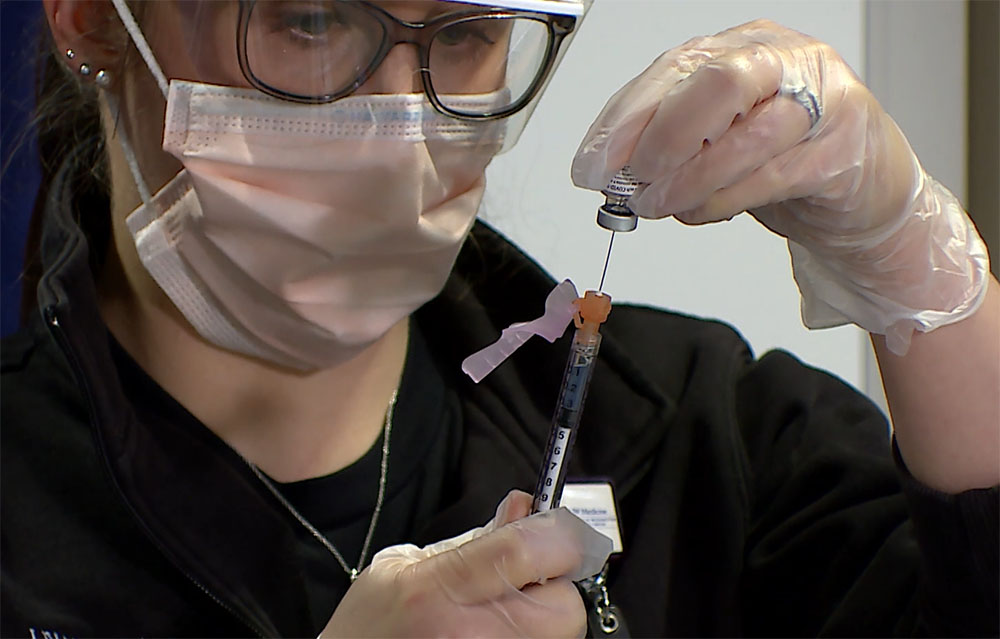 A nurse holding a syringe measuring a vaccine dose.