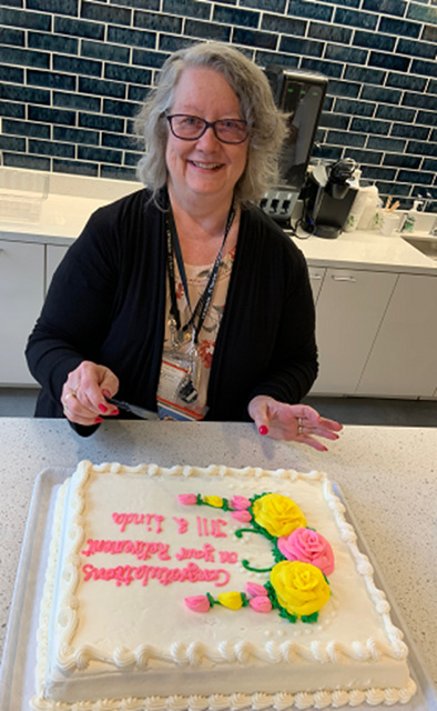 Linda Hays-Gallego smiling about to cut a cake at her retirement party