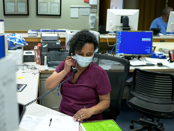 a masked nurse talking on the phone at a nursing station