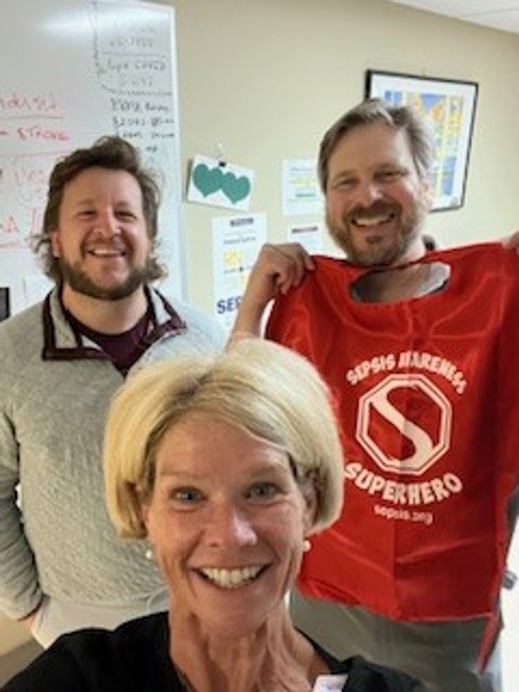 Sepsis awareness personnel smiling and holding up a sepsis awareness t-shirt