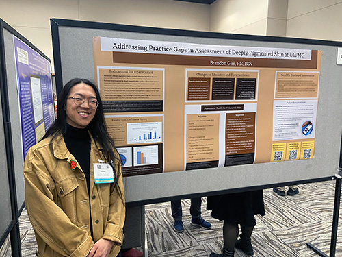 Poster presenter standing near poster titled Addressing Practice Gaps in Assessment of Depply Pigmented Skin at UWMC