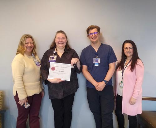 Amanda Stewart surrounded by colleagues holding her ROSE award.