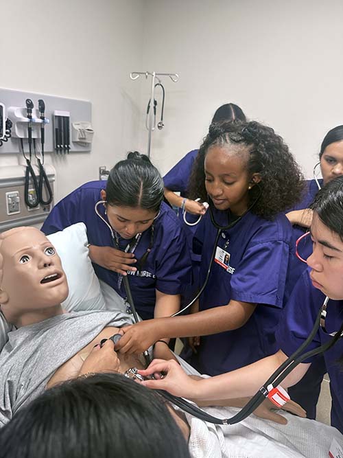 Nurse camp attendees gathered around a practice dummy checking vitals.