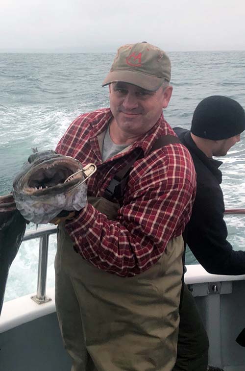 Wayne Lucey holding up a large fish while on a fishing boat.